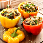 Three colorful bell peppers stuffed with a savory, anti-inflammatory vegan mixture of rice and herbs, garnished with chopped green onions and served on a wooden plate.