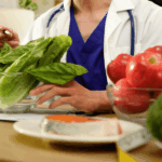 A doctor in blue scrubs examines lettuce, with apples, broccoli, and salmon on the table, suggesting a focus on healthy nutrition.