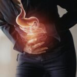 Person clutching their stomach in pain, with a glowing illustration of the stomach and intestines overlayed, indicating abdominal discomfort or digestive issues.
